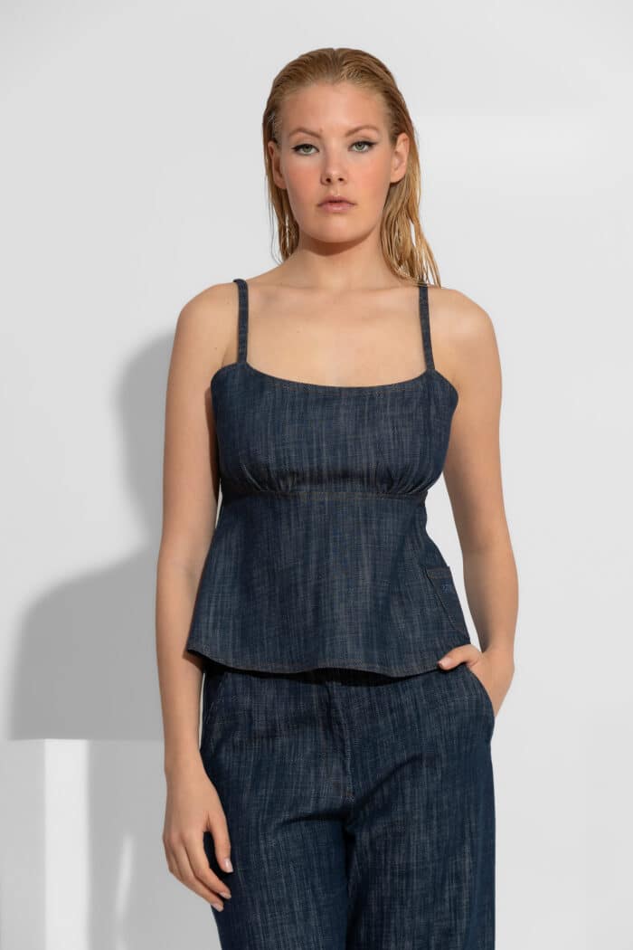 Empire Denim Camisole Top. A structured denim top featuring an empire waist, peplum hem, and adjustable open-back tie. 100% cotton. Made in Greece.